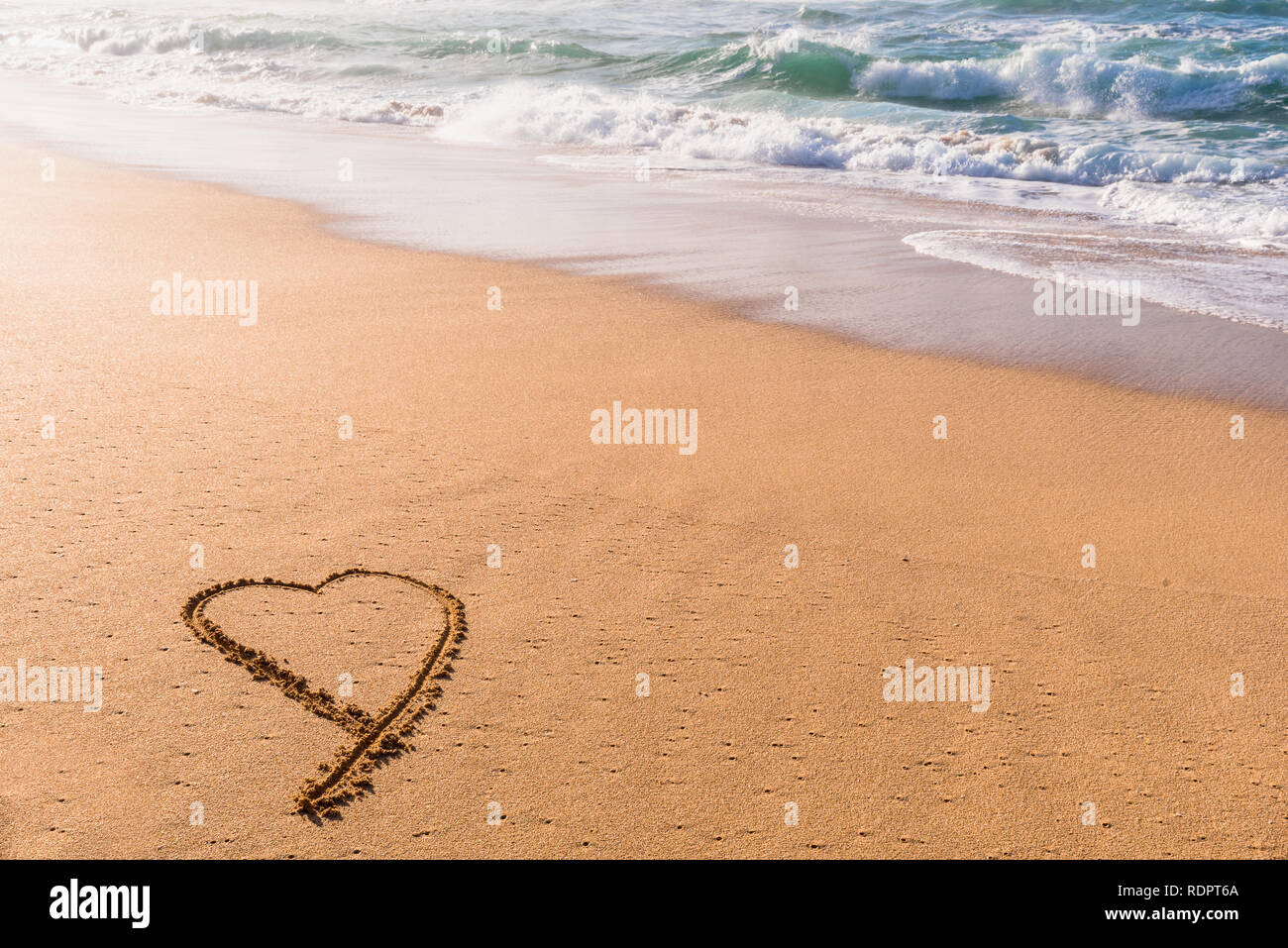 Heart drawn in the sand on the beach at sunset with waves washing in Stock Photo