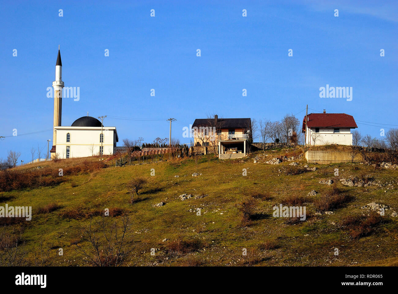 Bosnia and Herzegovina, outskirts of  Bihac. Two old country houses near a newly built mosque on a hill. Stock Photo