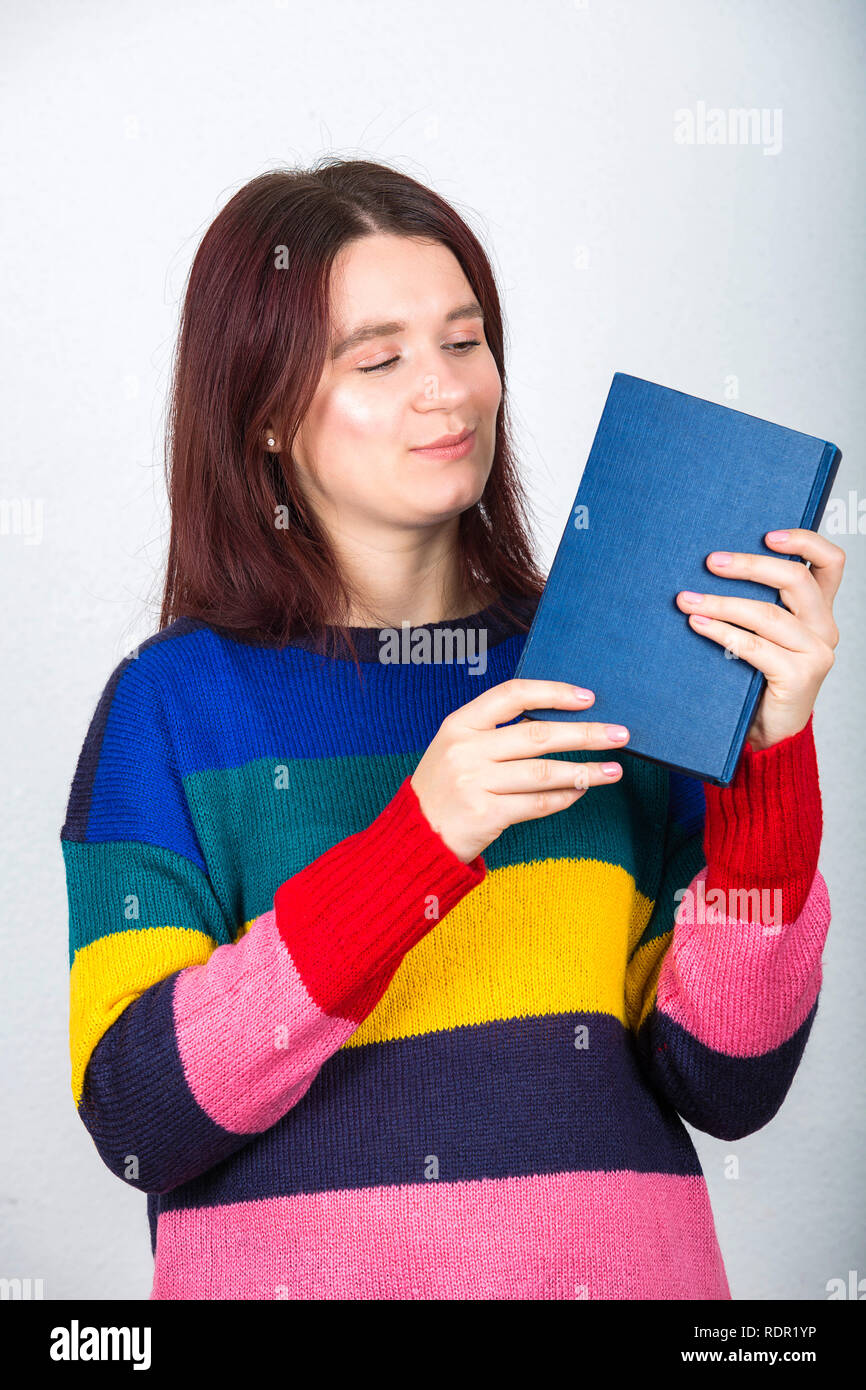 Young woman student holding a book in her hands looking attentive isolated over grey wall background. Stock Photo