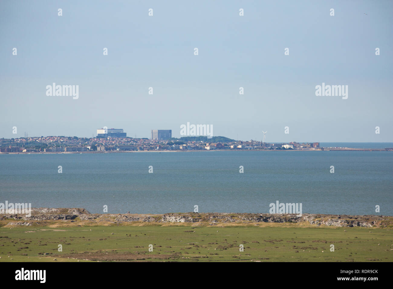 A view across saltmarshes on a hot and hazy day from Warton Crag of Heysham nuclear power station with part of Morecambe in the foreground. Lancashire Stock Photo