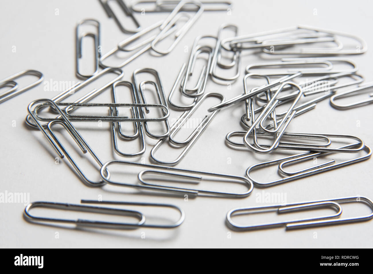 A close-up with selective focus of a bunch of metal paper clips scattered on a plain white background in horizontal image format. Stock Photo