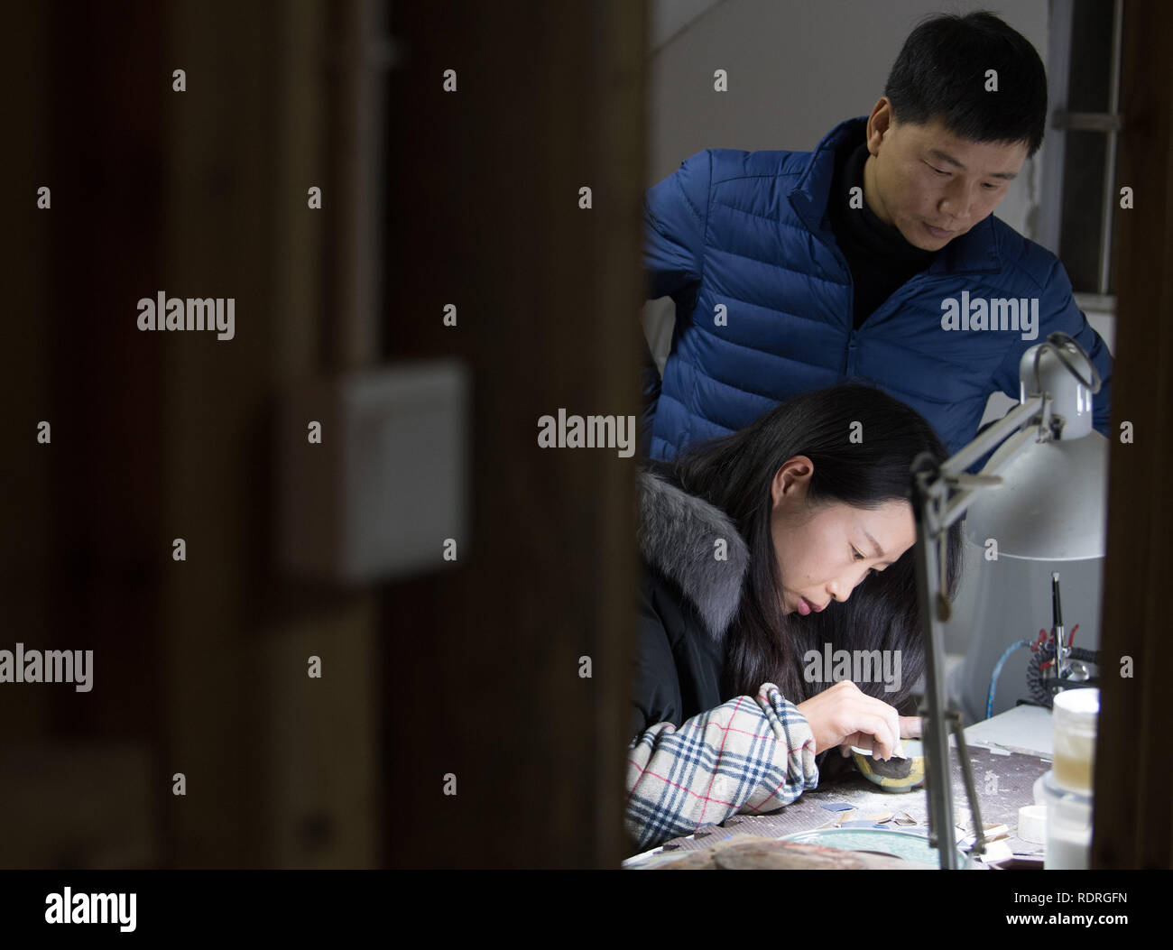 (190119) -- LONGQUAN, Jan. 19, 2019 (Xinhua) -- CHINA-ZHEJIANG-LONGQUAN-LACQUER ART (CN) Wu Rongqiang looks on as his wife Li shumin repairs a celadon ware with lacquer at his studio in Niutouling Village, Longquan City of east China's Zhejiang Province, Jan. 15, 2019. Wu Rongqiang, a Longquan native aged 45, started exploring traditional lacquer art since 2012. In 2017, he moved his family to an old house deep in the mountains in Longquan in order to do more experiments in lacquer undisturbed. He uses lacquer to repair broken porcelain and to create lacquerware. Also, he experimen Stock Photo