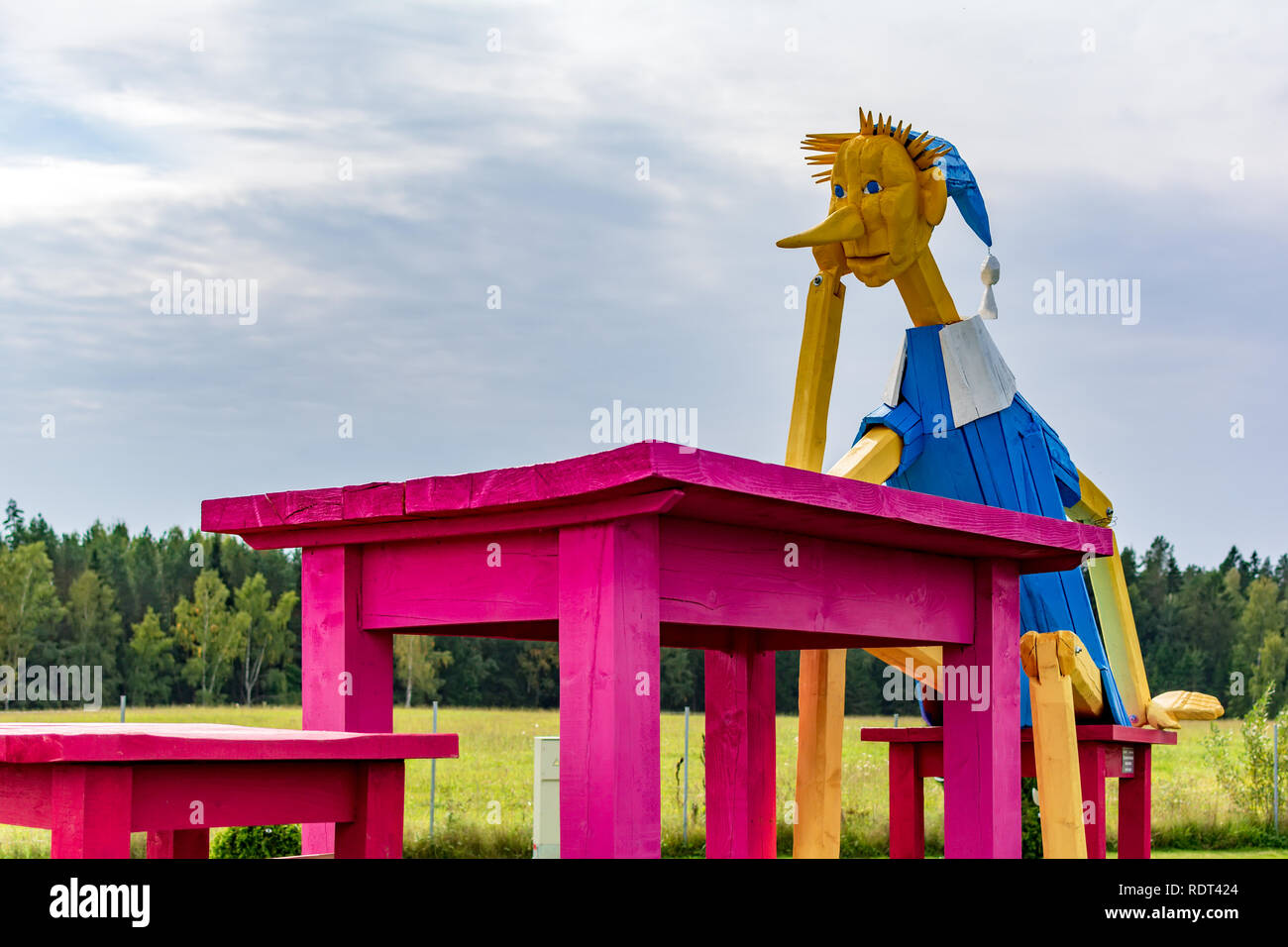 Anyksciai, Lithuania - September 8, 2018: Giant wooden Buratino (Pinocchio) sitting reflective at the enormous pink table in the park. Stock Photo