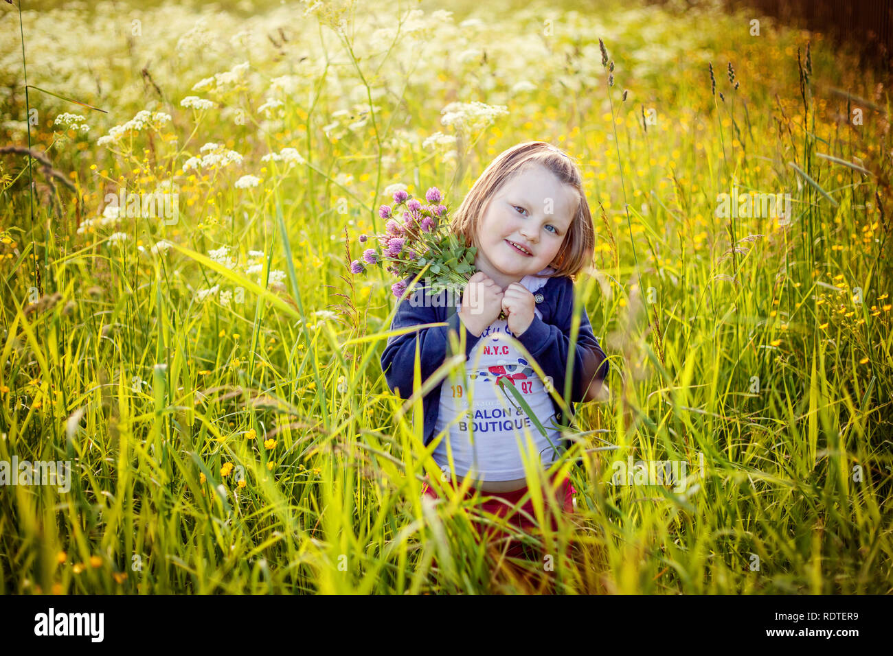 Happy cute little girl standing on meadow with wild flowers in park or ...