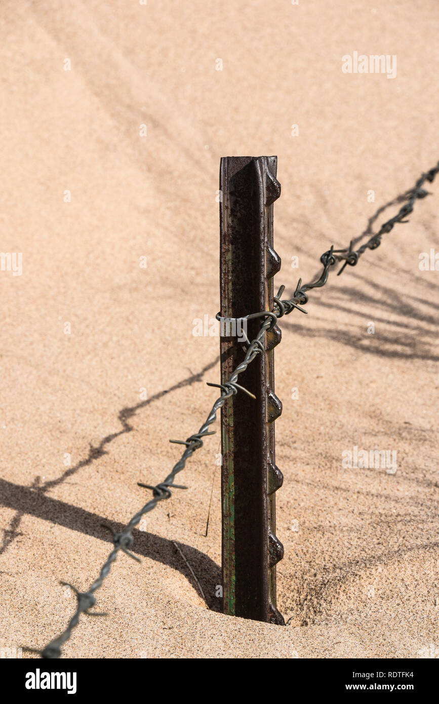 Barbed wire fence with metal posts nearly buried in sand Stock Photo