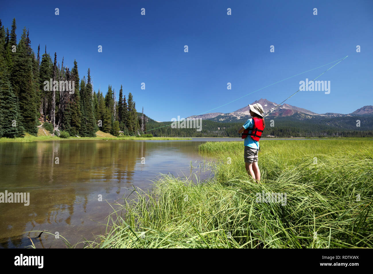 Girl fishing from shore along channel at Sparks Lake, Broken Top Mountain in background, Cascade Lakes, Oregon, USA Stock Photo