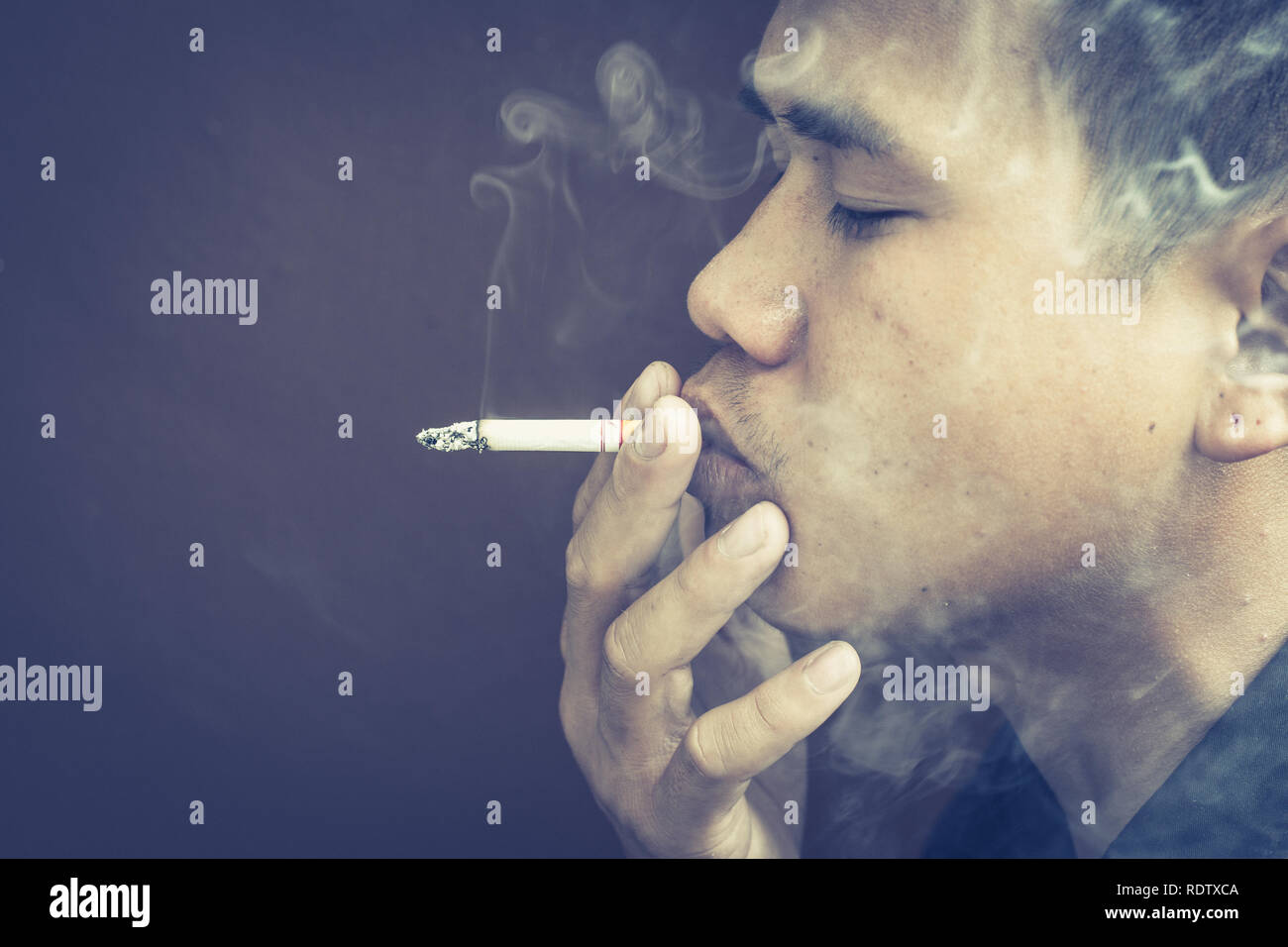 Side view of young man is smoking against black background. Stock Photo