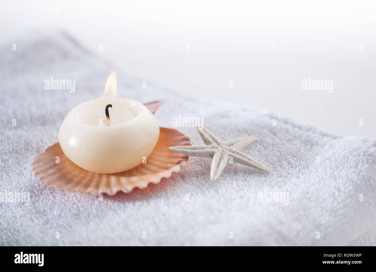 Lit-up candle with natural shells placed on white towel. Stock Photo