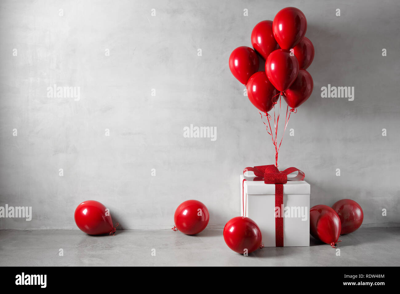Red balloons and white gift box on concrete wall background Stock Photo
