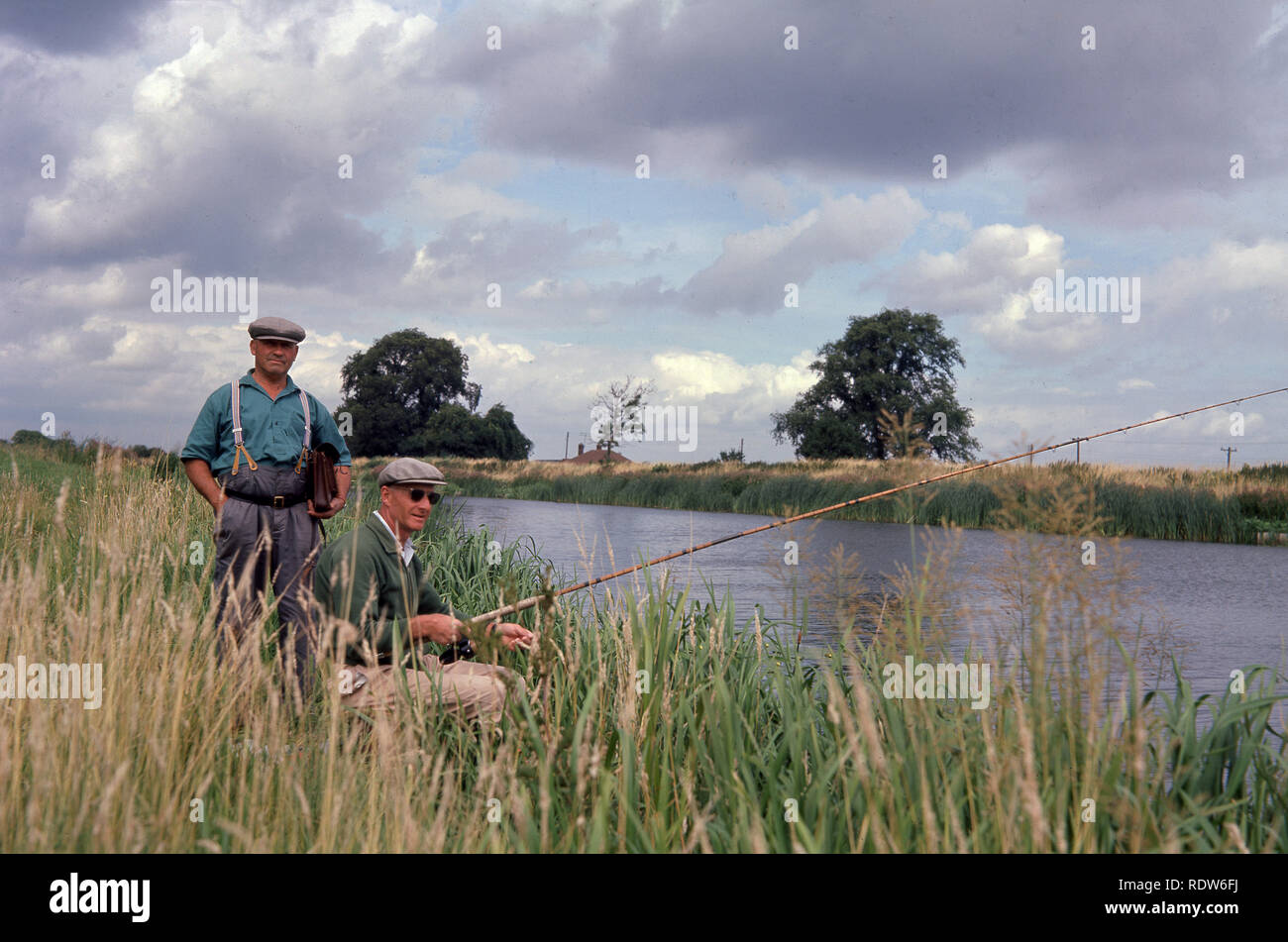 1960s, two anglers on the river Great Ouse, Norfolk, England, UK, fishing from the rushes on the riverbank. At 143 miles in length, it is the longest of several British rivers called 'Ouse' and one of the longest in the UK. Stock Photo