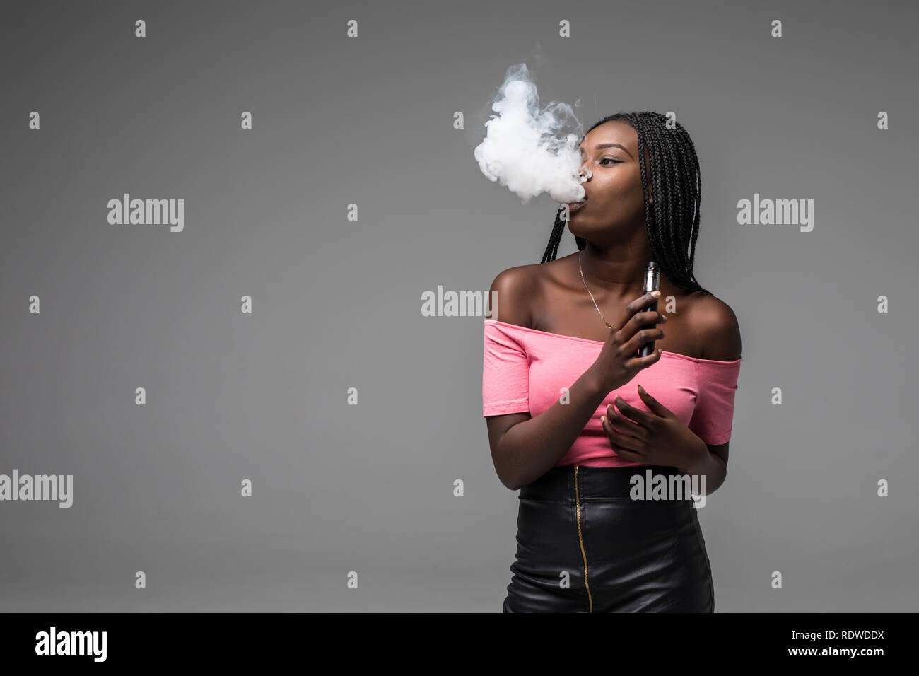 Portrait of young african woman standing with vape device in hand on gray background Stock Photo