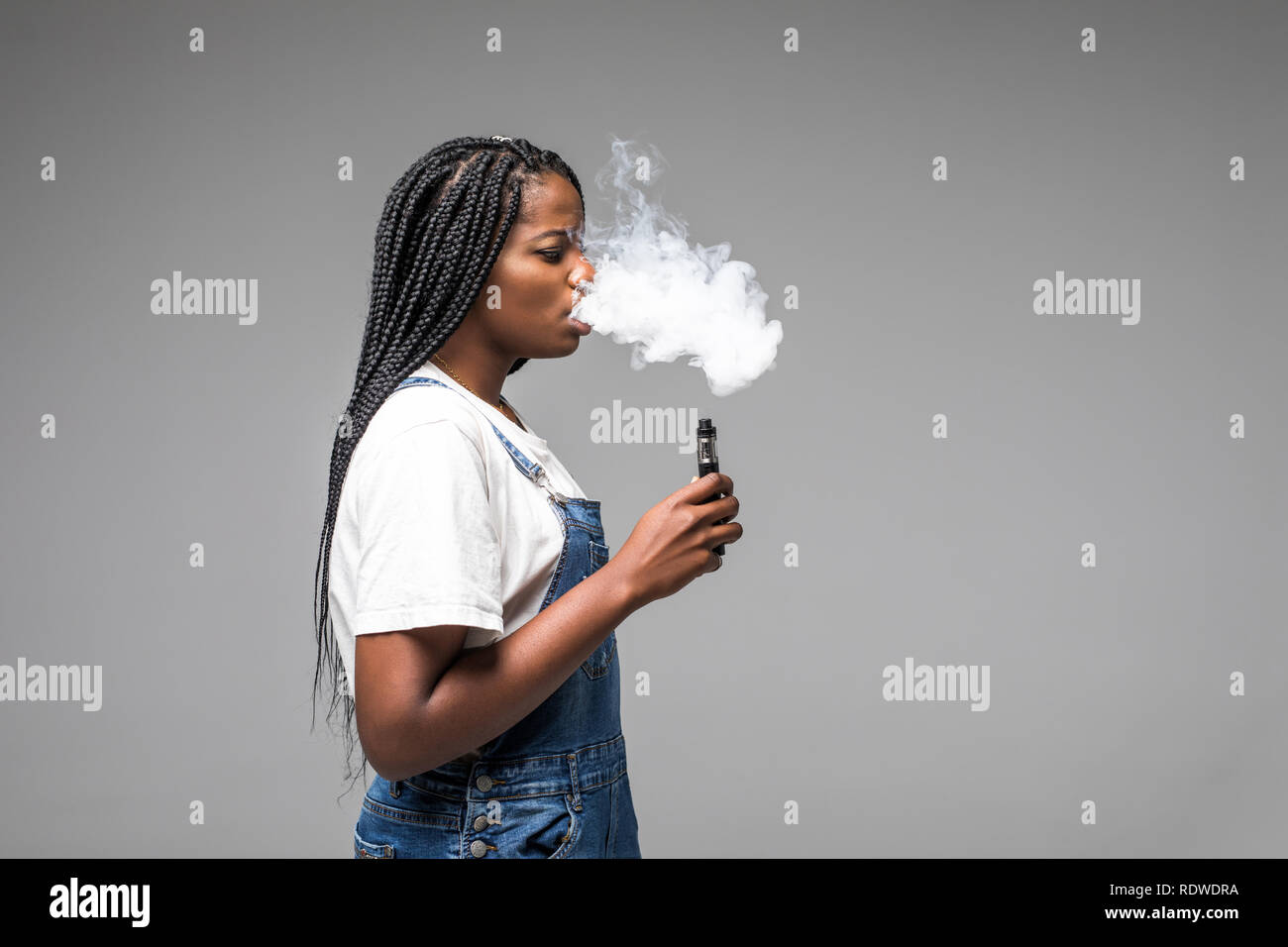 Side view portrait of guy holding vape device and exhaling cloud of smoke isolated on blue background. Stock Photo