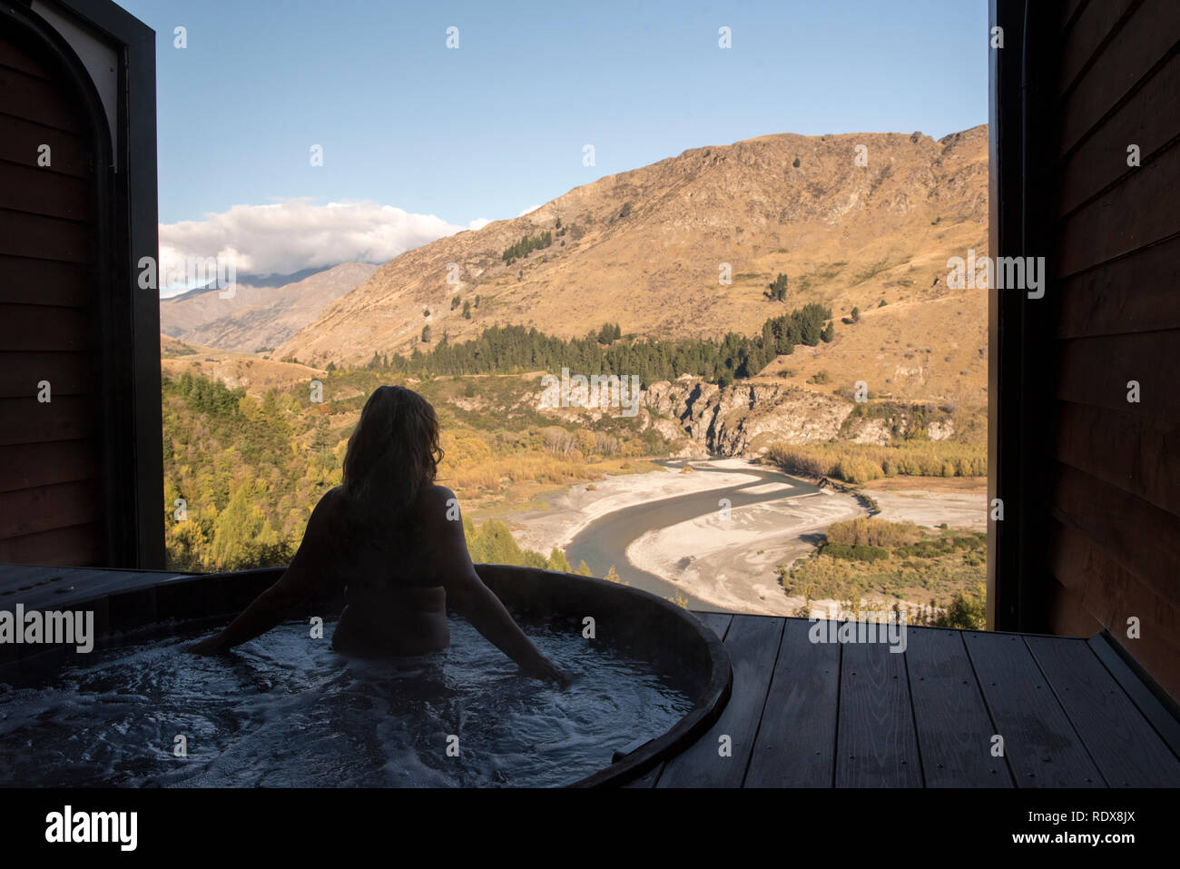 A woman (model released) relaxes in a hot tub while enjoying views of the Shotover River at the Onsen Hot Pools near Queenstown, New Zealand. Stock Photo