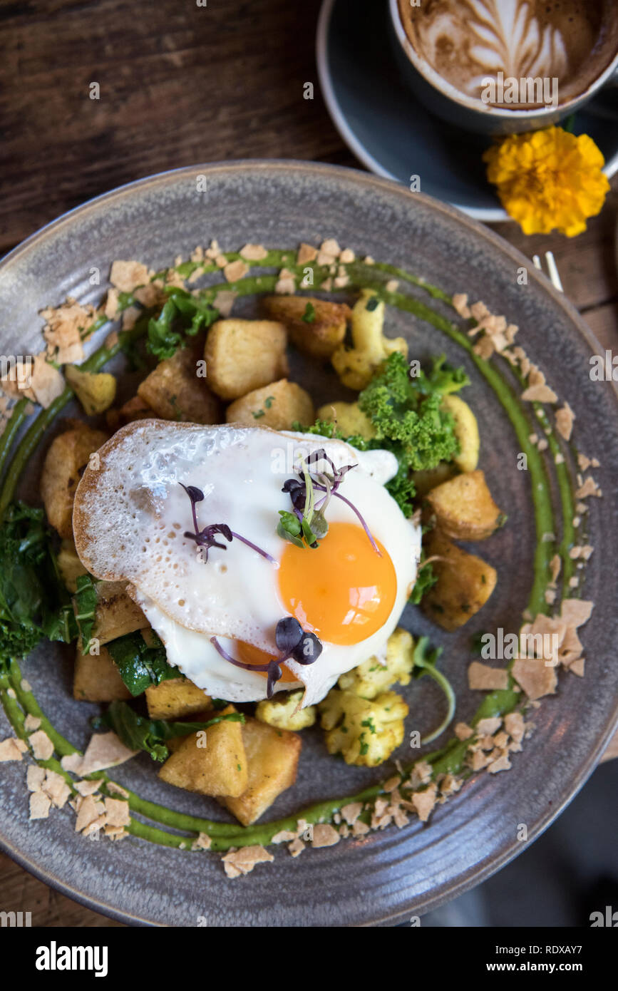 Veggie hash with potatoes, kale, and cauliflower topped with two fried eggs. Bespoke Kitchen is a popular restaurant located on the road up to the gon Stock Photo