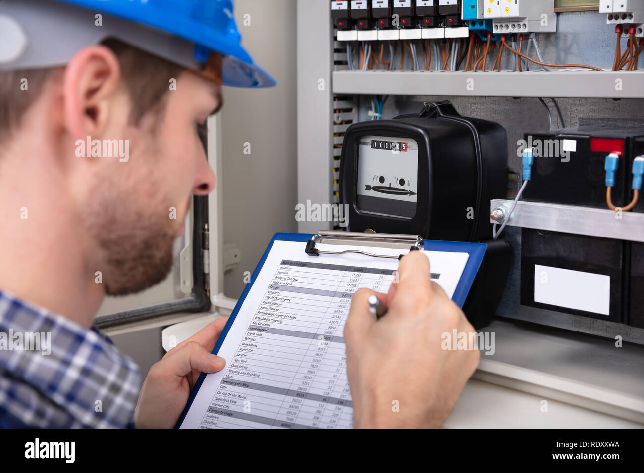 Close-up Of Male Technician Writing On Clipboard In Front Of Fuse Box Stock Photo