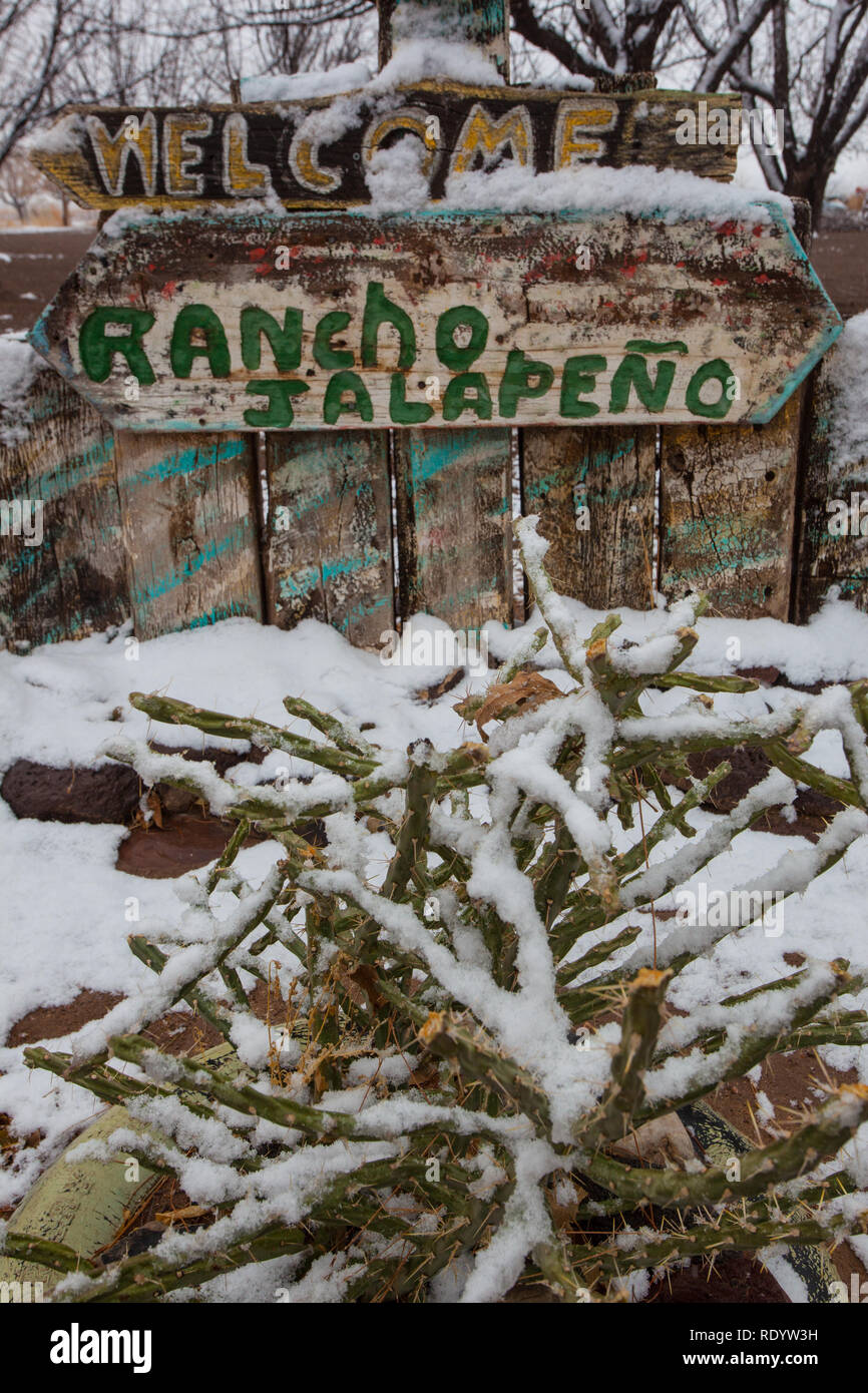 A splattering of snow around desert plants and a farm sign in the Mesilla Valley of New Mexico Stock Photo