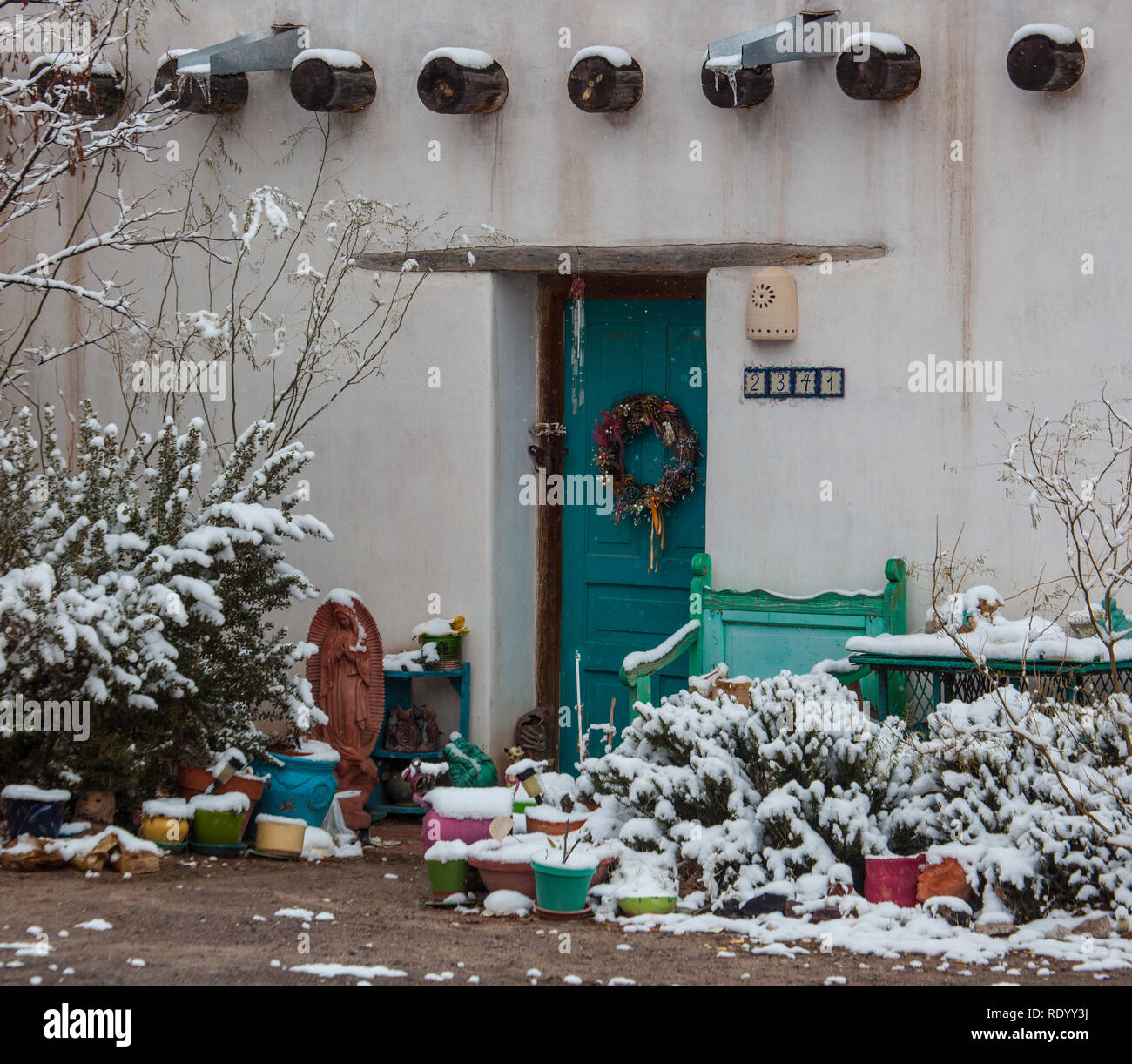 Snow Covers Bushes Beside A Turqoise Door On A Historic Adobe Home