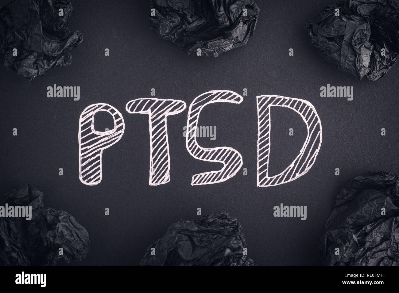 Post Traumatic Stress Disorder. Abbreviation PTSD on a black background and black crumpled paper balls around it. Close up. Stock Photo
