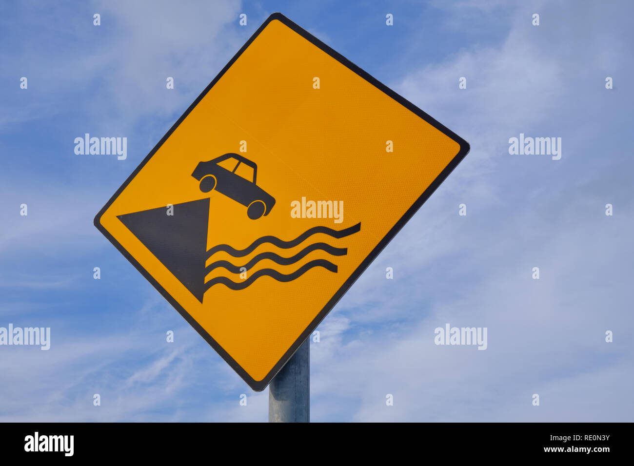 Sign Caution Car falling from Pier.  Diamond shape, yellow background on an angle against blue and clouds Stock Photo