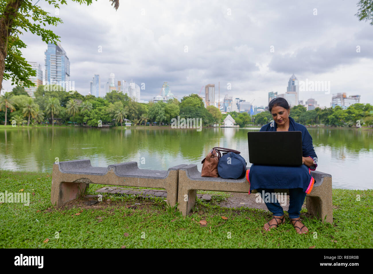Portrait of mature Indian woman at park using laptop computer Stock Photo