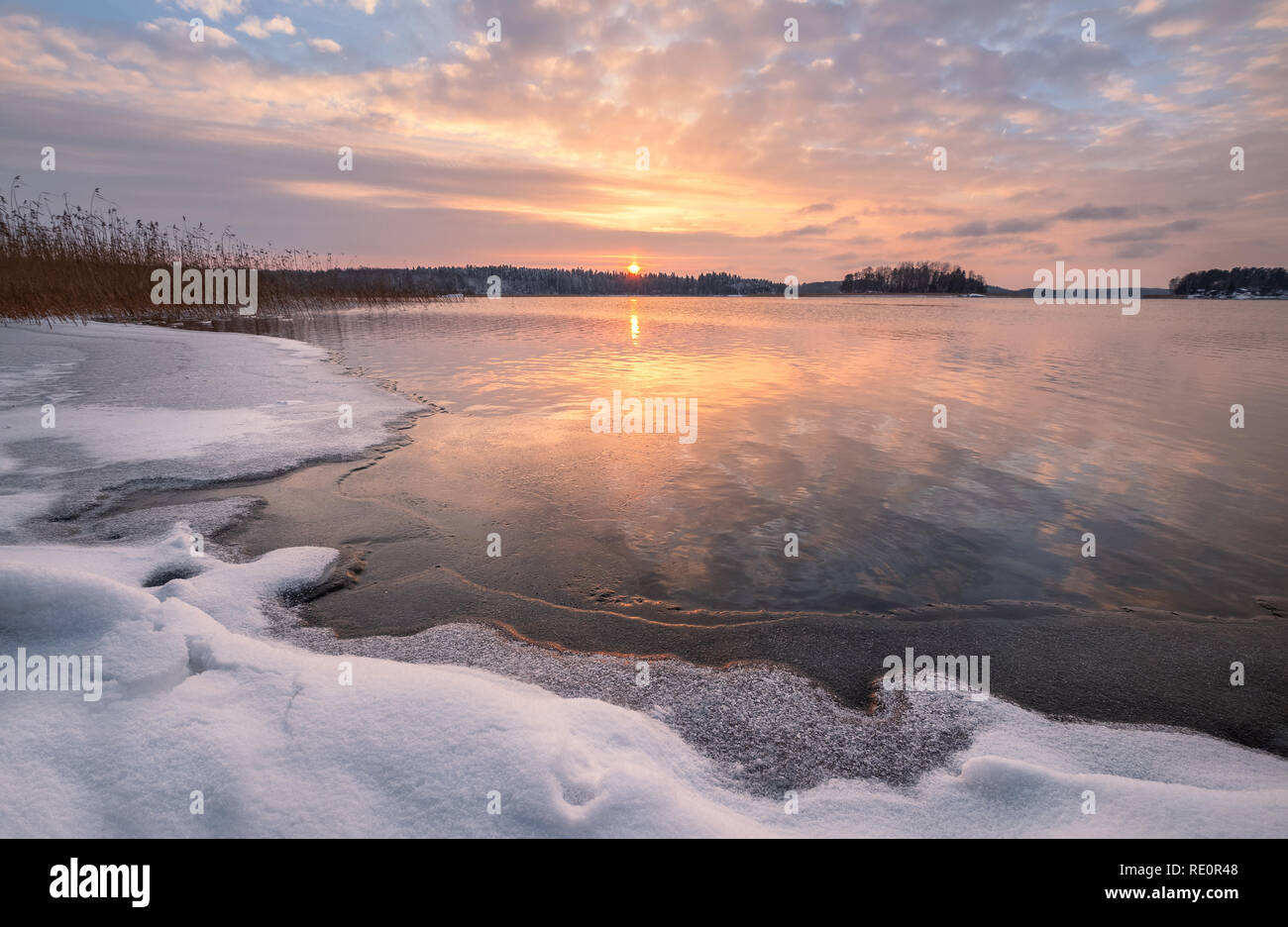 Scenic winter landscape with frozen lake and sunset at evening time in Finland Stock Photo