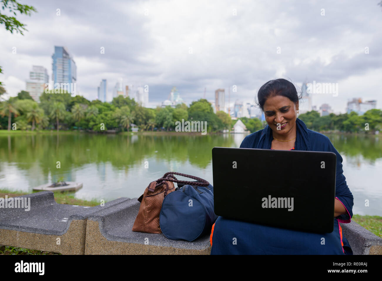 Portrait of mature Indian woman at park using laptop computer Stock Photo