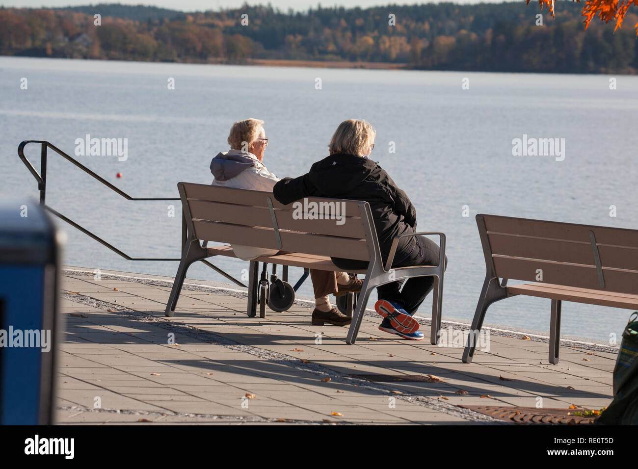 LADIES ON BENCH by the water talking in the autumn sun Stock Photo