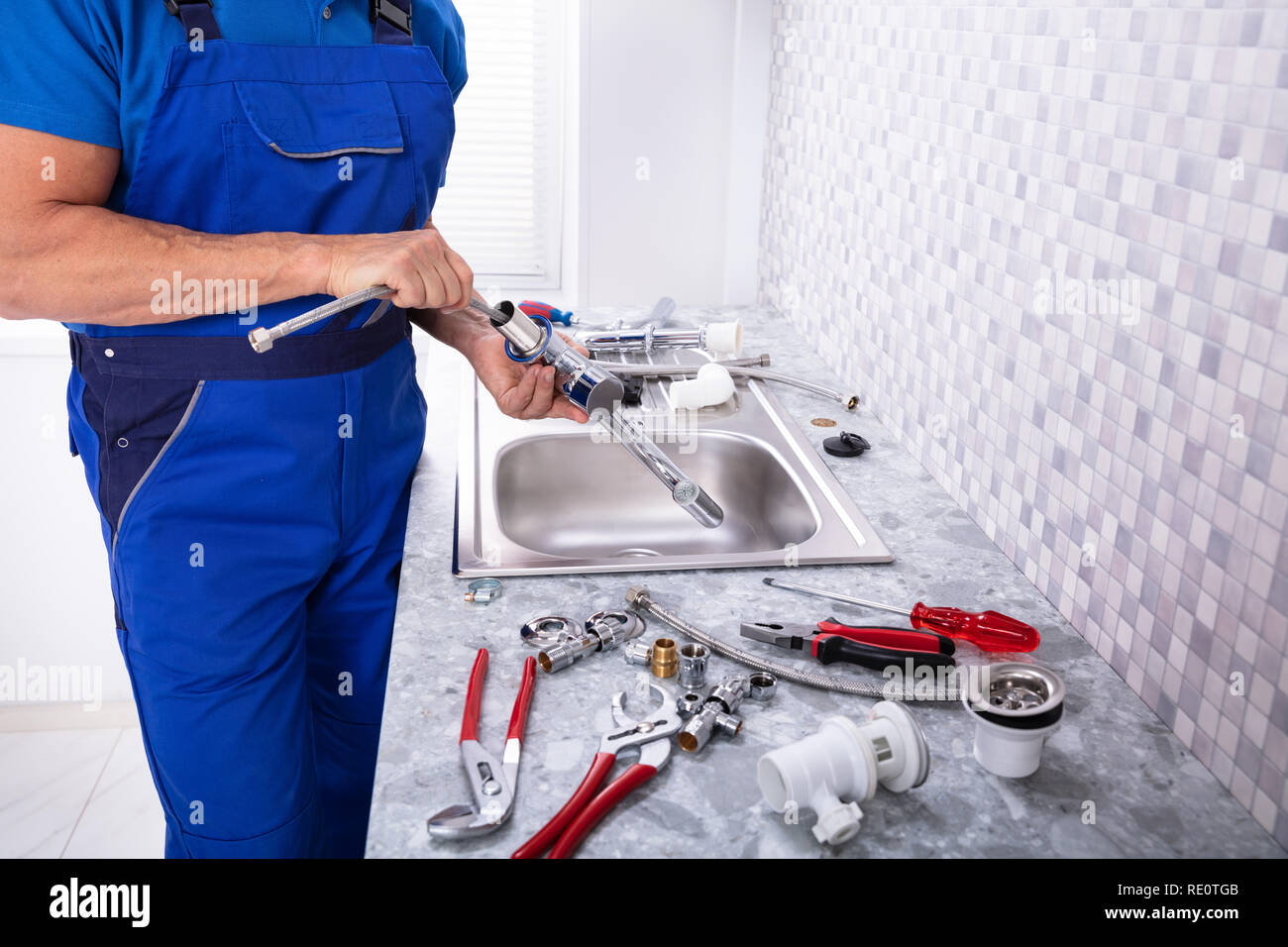 Side View Of A Plumber Fixing Water Tap In Kitchen Stock Photo