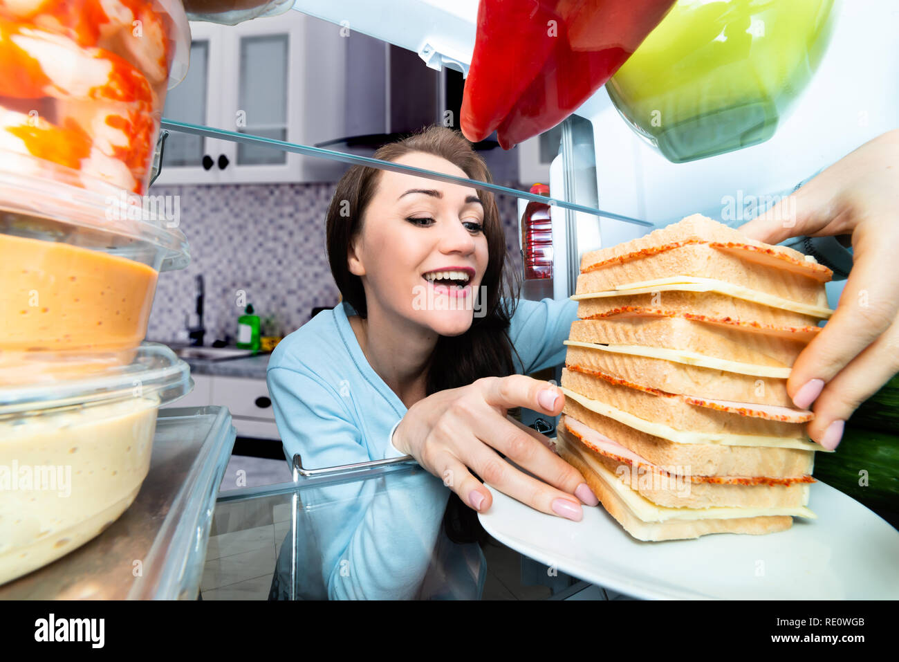 Happy Young Woman Taking Big Sandwich From Refrigerator Stock Photo