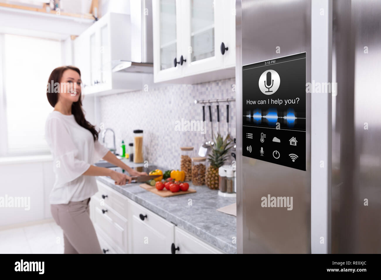 An Oven With Voice Recognition Function Near Smiling Young Woman Cutting Vegetables In Kitchen Stock Photo