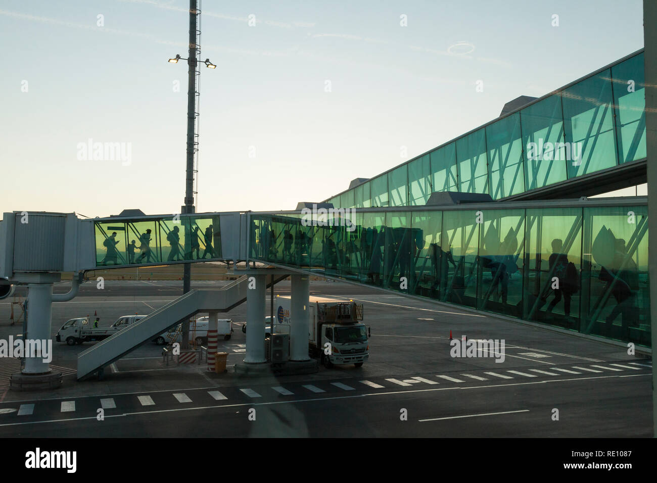 Passengers disembarking from a flight at dawn, Cape Town International Airport sihouetted against a colorful sky in the walkway connecting the plane t Stock Photo