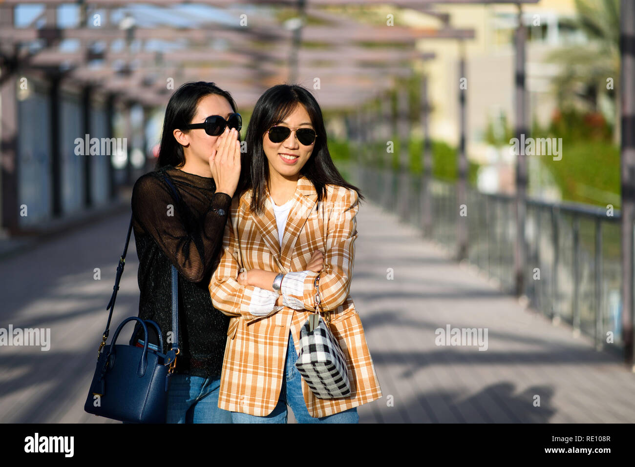 Two female friends sharing secrets on the street Stock Photo