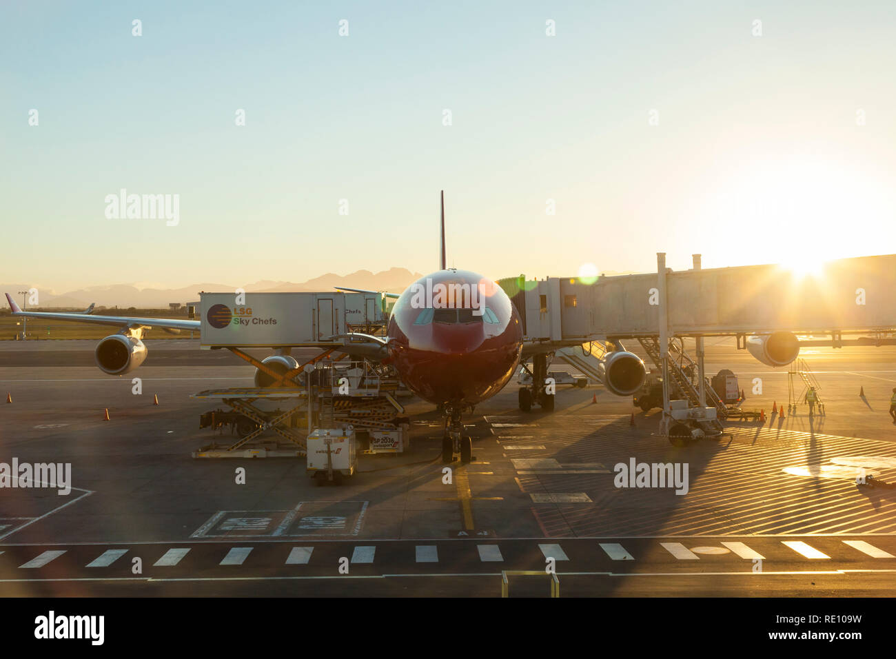 Early morning dawn arrival of Edelweiss airplane at Cape Town International Airport with sunburst and flare. Personnel on the ground Stock Photo