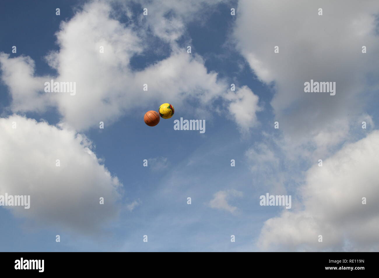 2 balls flying through the air side by side with Blue sky and White clouds. Clear image could be used as a book cover. Concept. Conceptual Book cover. Moody book cover. What's that all about book cover. Sky. Bright with plenty of space for Title and Author's name. Stock Photo