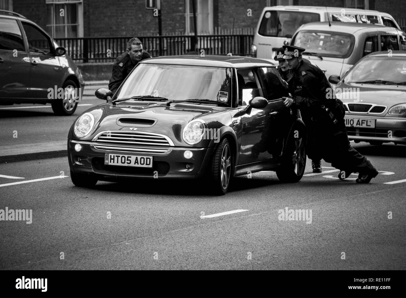 Three British police officers in uniform pushing a Mini Cooper after a break down from the right lane towards a more suitable spot - London, UK Stock Photo