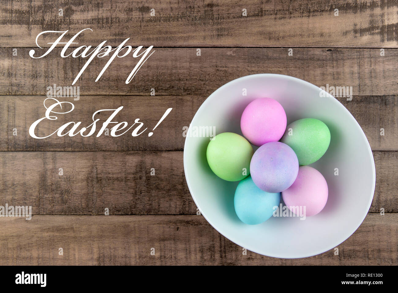 Overhead view of pastel painted easter eggs in a white bowl on rustic ...