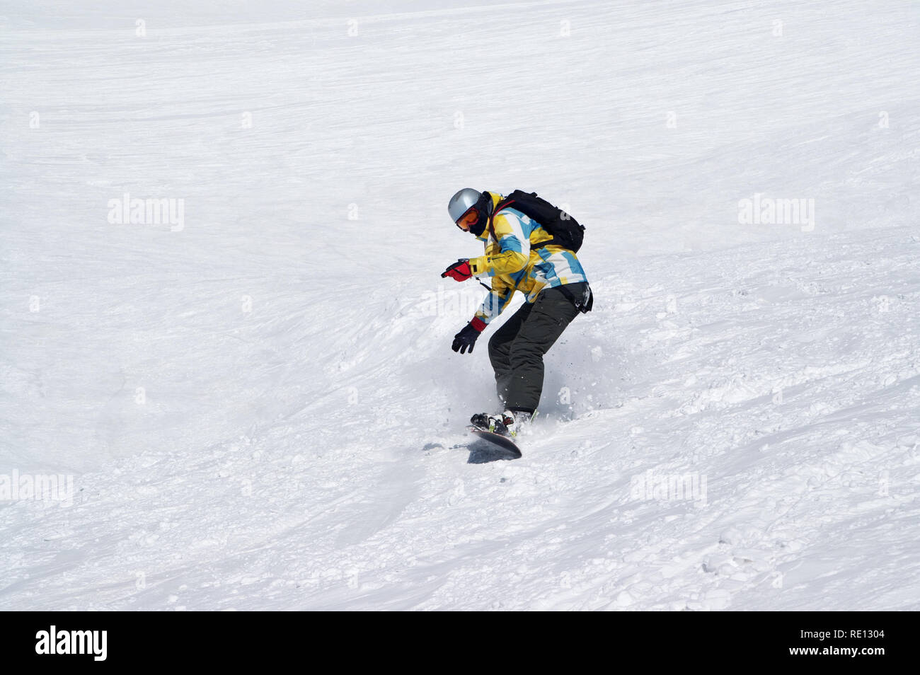 Snowboarder downhill on snowy ski slope at high winter mountains in sun ...