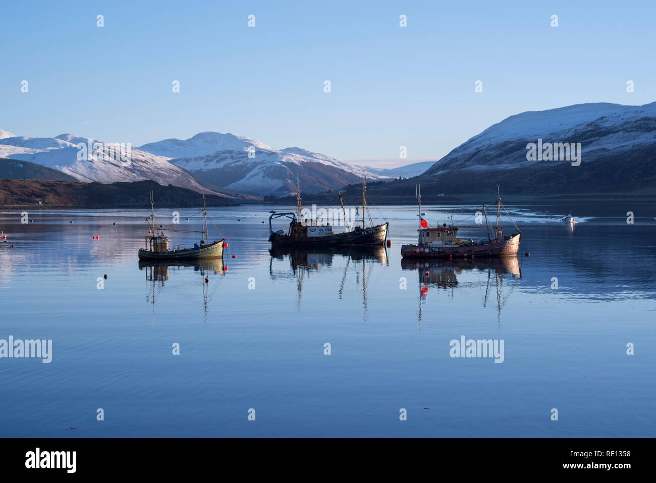 Fishing boats reflections moored in Loch Broom, Ullapool, with snowy winter mountains in the background Stock Photo