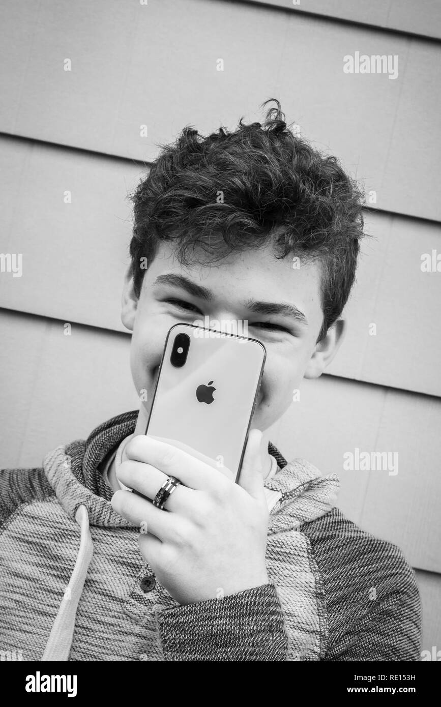 Male teenager holding up his new iPhone X in front of his face, big smile Stock Photo
