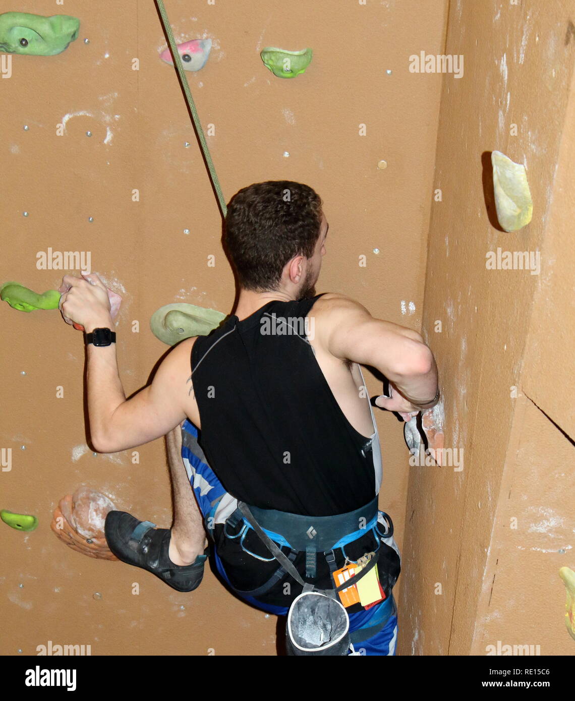 Climber pushing against a hold while ascending brown wall Stock Photo