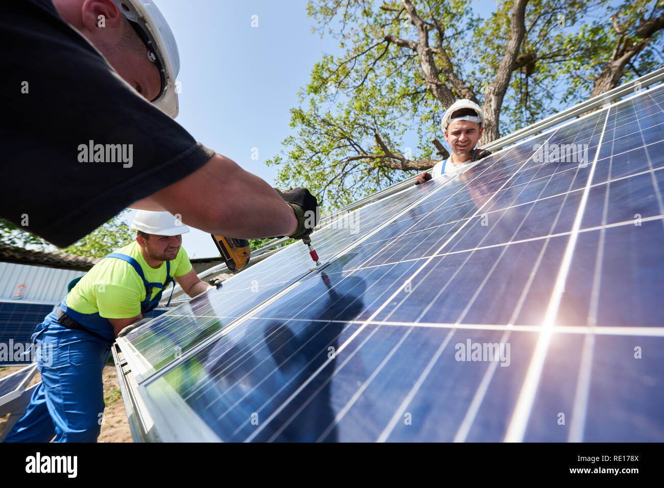 Team of three technicians working on exterior voltaic solar panel system installation in rural countryside on bright sunny summer day. Renewable ecological cheap green energy production concept. Stock Photo