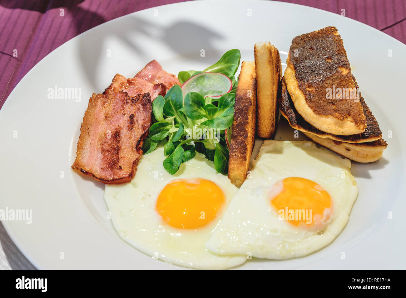 American breakfast with sunny side up eggs, bacon and french toast, close up photo. Stock Photo