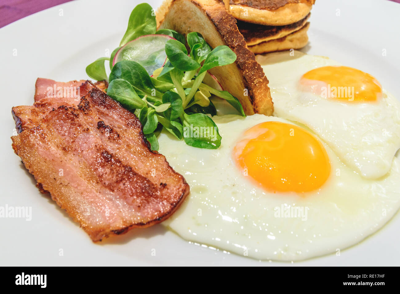 American breakfast with sunny side up eggs, bacon and french toast, close up photo. Stock Photo