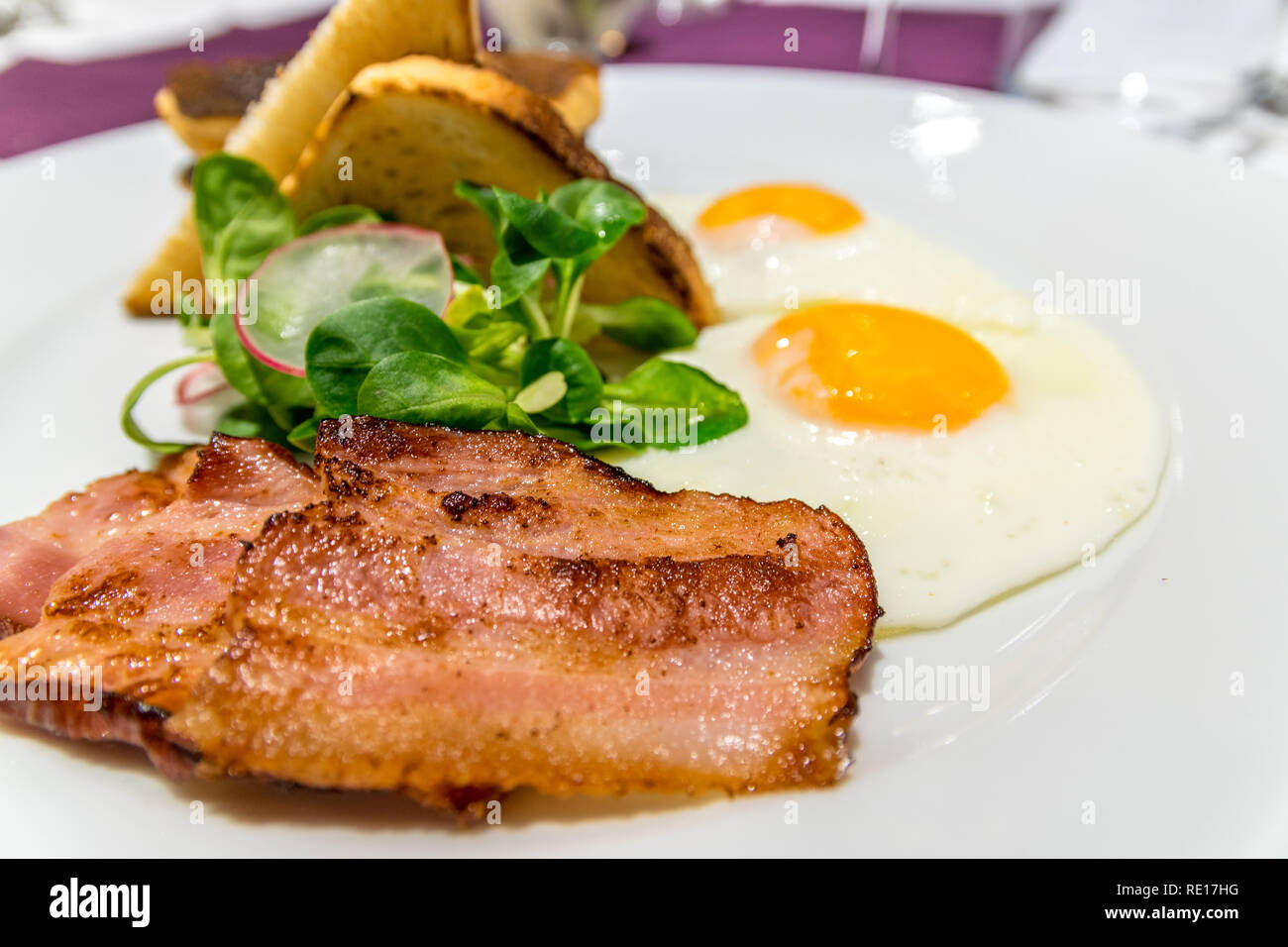 Bacon on an American breakfast plate with sunny side up eggs and french toast, close up and selective focus photo. Stock Photo