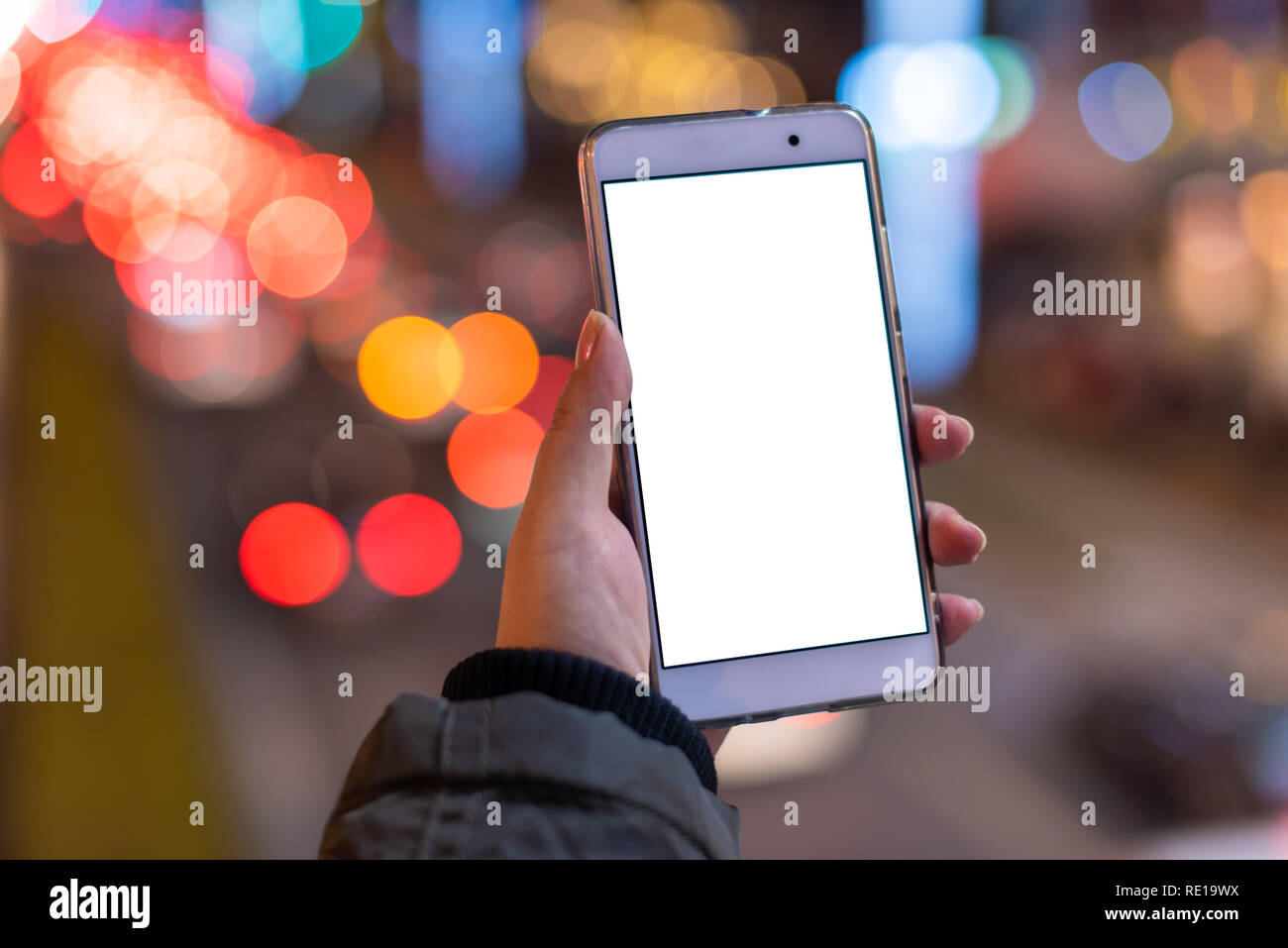 Woman holding a smartphone with a blank white screen at night with lights from car traffic in the background Stock Photo