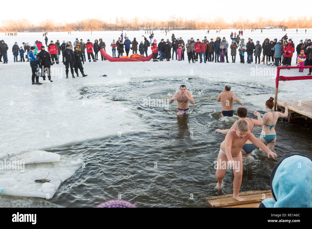 Boy climbs on wooden steps from chilly water on a freezing winter day 19 January -  Jesus Water Baptism in Kiev - as others enter the chilly water Stock Photo