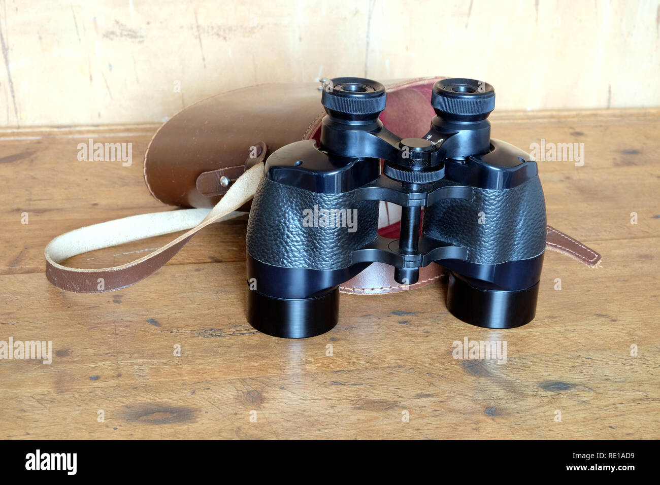 Vintage english military prism black color binoculars and opened brown hard leather carry case on wooden background front view closeup Stock Photo