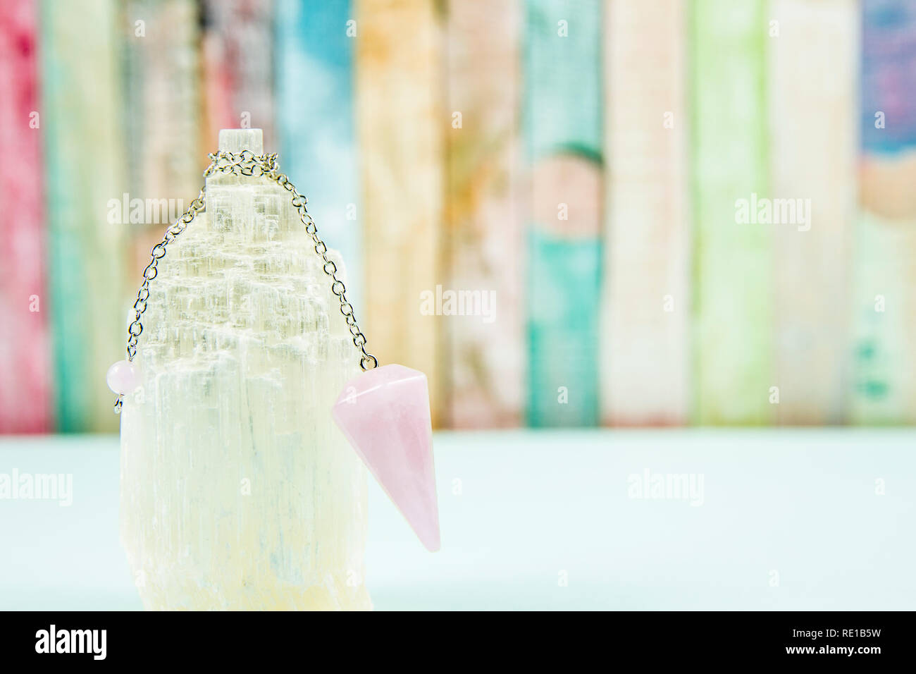 Using crystal Selenite tower for loading rose quartz pendulum, light blue table and pastel color wooden board background. Divination, fortune telling Stock Photo