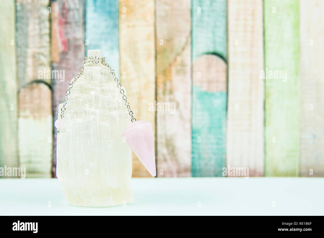 Using crystal Selenite tower for loading rose quartz pendulum, light blue table and pastel color wooden board background. Divination, fortune telling Stock Photo