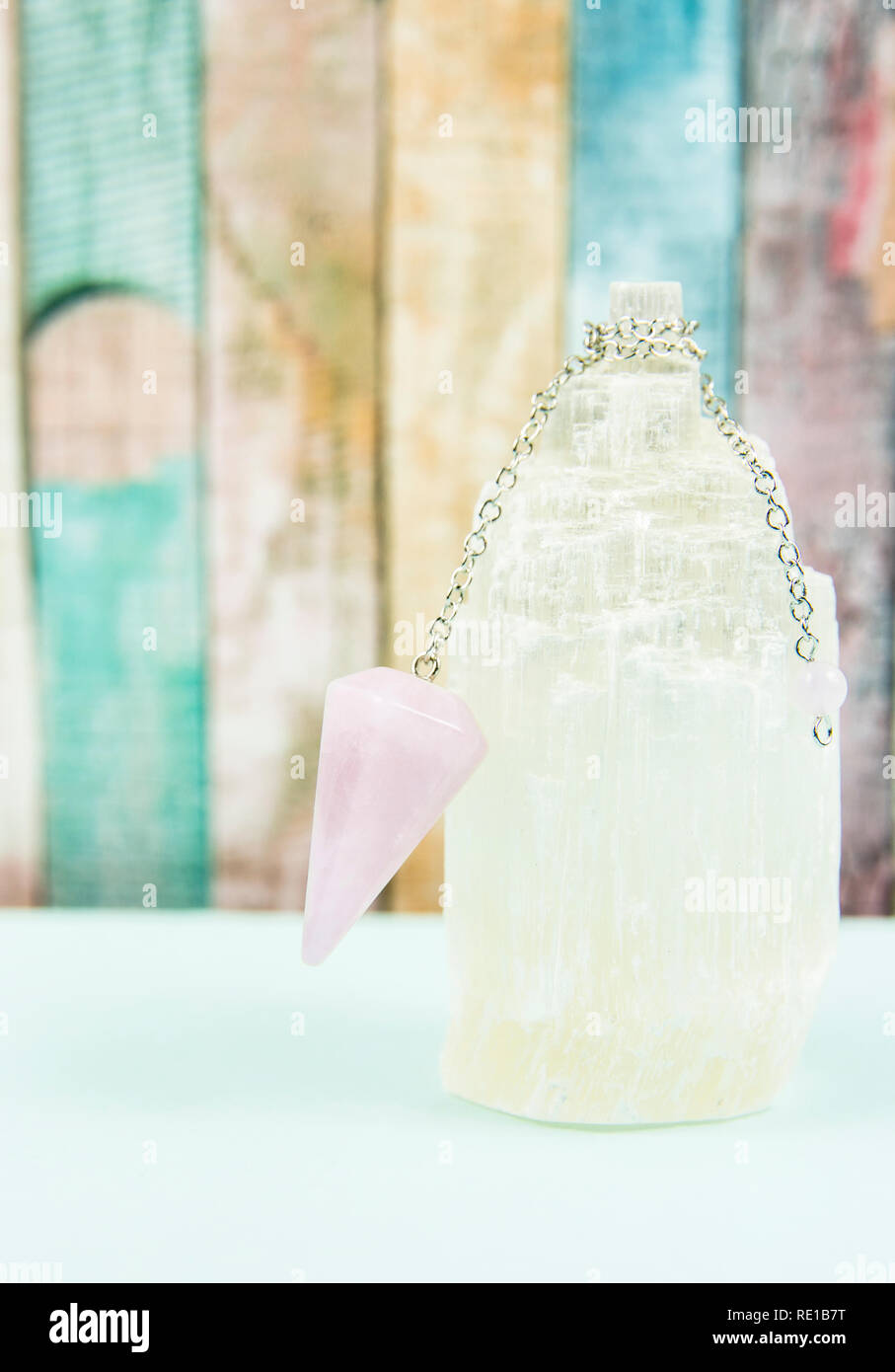 Using crystal Selenite tower for loading rose quartz pendulum, light blue table and pastel color wooden board background. Divination, fortune telling Stock Photo